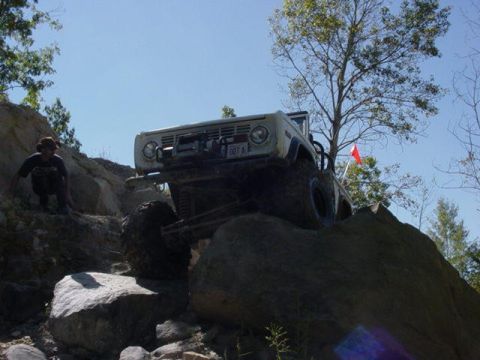 1992 Ford Bronco - This white off-road SUV navigates a rocky incline, its front end prominently displayed with a license plate reading '007 A'.