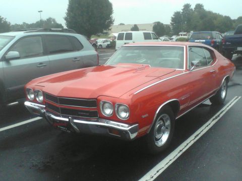 1988 Ford Bronco - This classic red Chevrolet Chevelle is parked in a lot, with a silver SUV beside it.