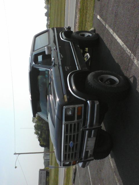 1988 Ford Bronco - This black Ford Bronco is parked in a lot with a road and grassy area in the background.