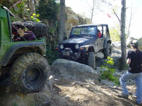 1992 Ford Bronco - Two off-road Jeeps tackle a challenging rocky trail in a wooded area.