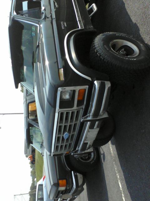 1988 Ford Bronco - A black SUV with a prominent chrome grille is parked next to another vehicle.
