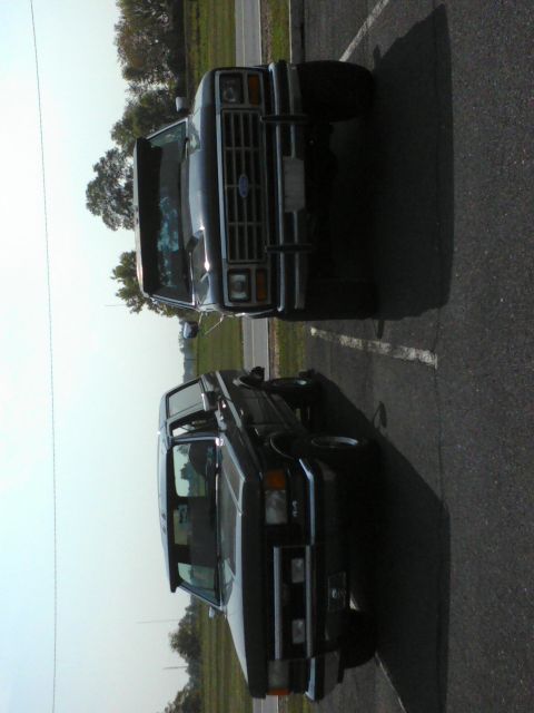 1988 Ford Bronco - Two Ford Broncos are parked in a lot. The front vehicle is visible from the front.
