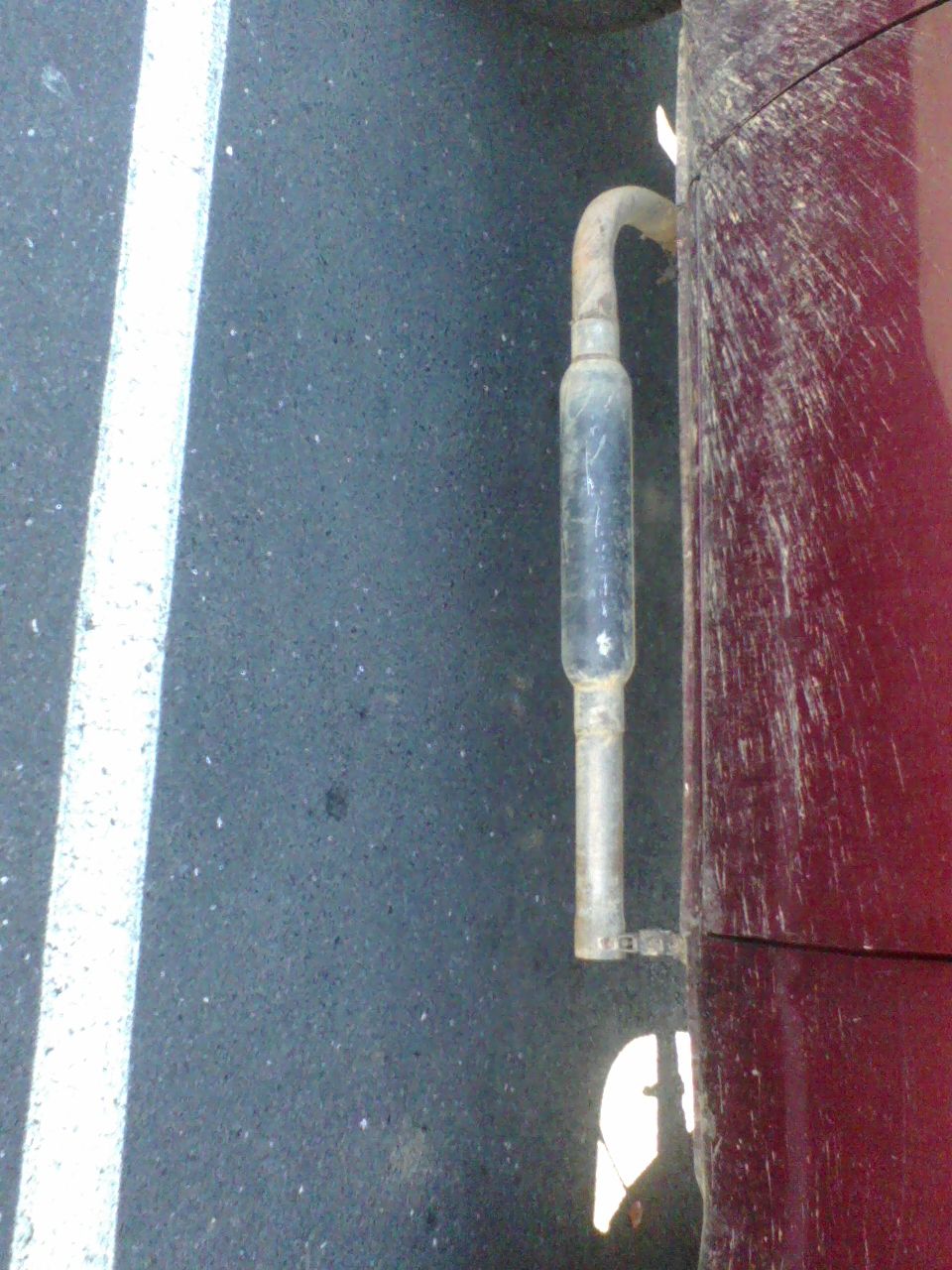 Close-up of a vehicle's exhaust pipe exiting near the rear side panel. The panel is red and appears dirty