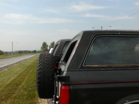 1988 Ford Bronco - Two 1988 Ford Broncos are parked on the side of the road under a partly cloudy sky.