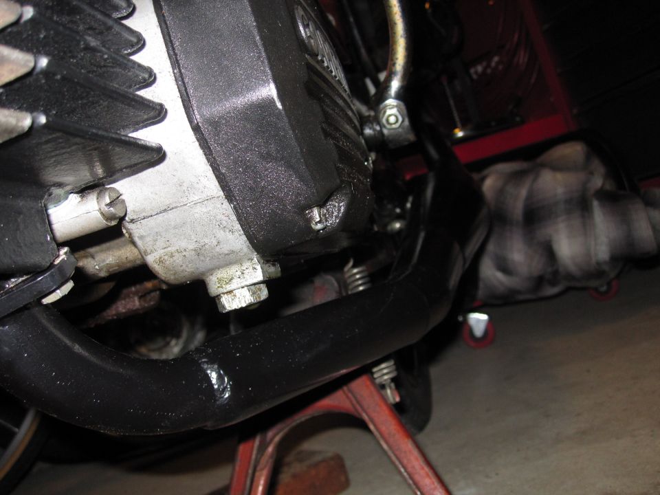 Motorcycle engine with black exhaust pipe on a red stand. A person in a plaid shirt is visible