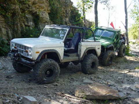 1992 Ford Bronco - A white 1992 Ford Bronco, equipped with large off-road tires, is parked on a rocky trail next to a green off-road vehicle.