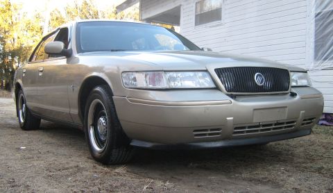 2000 Mercury Grand Marquis - This gold sedan is parked on a dirt lot in front of a white building.