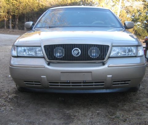 2000 Mercury Grand Marquis - The front grille and headlights of a gold 2000 Mercury Grand Marquis are visible.