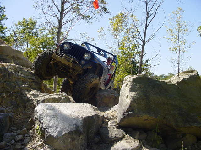 Jeep Wrangler climbing over large rocks on a trail. Driver is visible