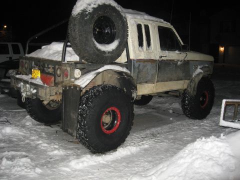 1990 Ford F-250 - A heavily modified pickup truck sits in the snow at night, equipped with oversized tires and a spare tire carrier.