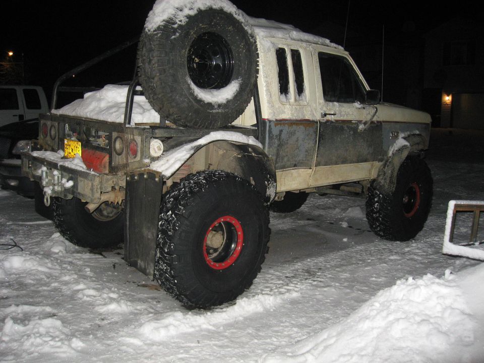 Pickup truck with large tires and a spare tire mounted on the back, covered in snow