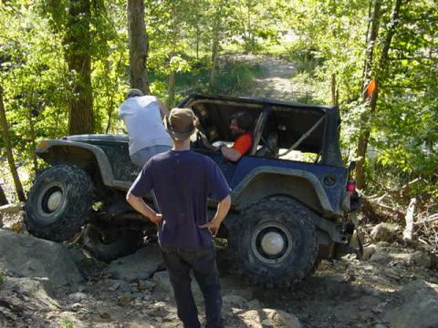 1992 Ford Bronco - A blue Jeep Wrangler is shown off-roading on a challenging rocky path with onlookers.
