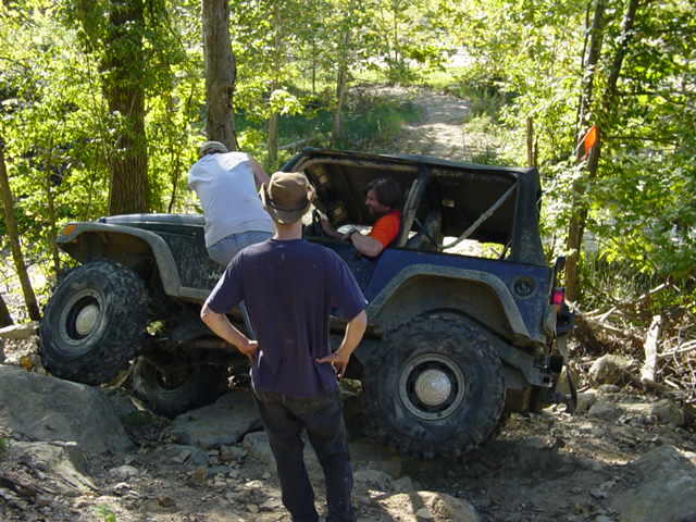 Blue Jeep Wrangler navigating a rocky trail with people inside and watching