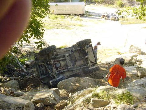 1992 Ford Bronco - An off-road vehicle has overturned on a rocky terrain, with two onlookers present.