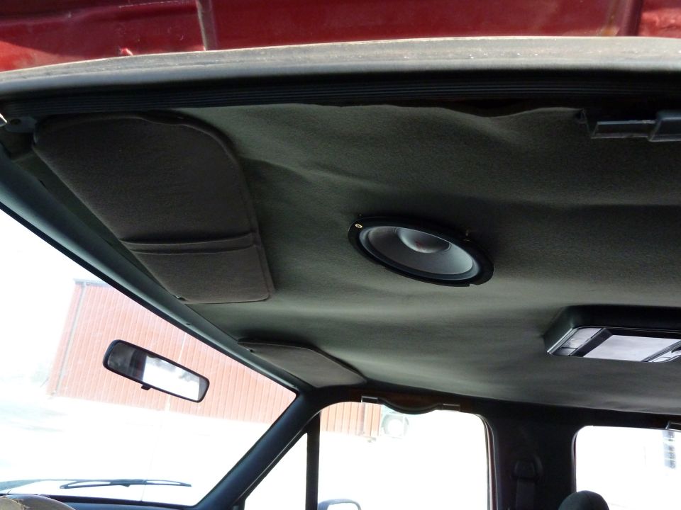 Interior shot of a vehicle's headliner with a speaker installed and a sun visor. A rearview mirror is visible