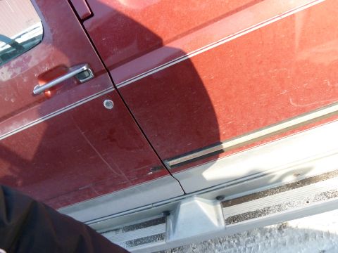 1993 Ford C-150 (Centurion Conversions) - Side view of a red truck door and running board, showing chrome trim and a shadow across the panel.