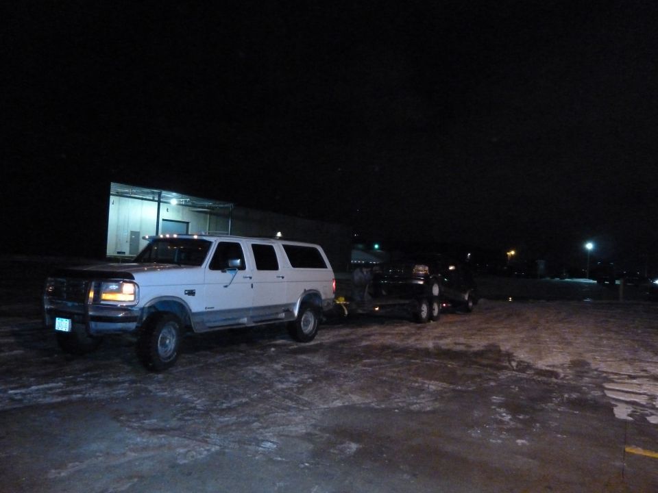 White extended cab pickup truck towing a trailer at night
