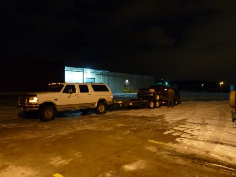 1993 Ford C-150 (Centurion Conversions) - A white Ford F-250 Super Duty tows a trailer carrying a dark SUV at night.