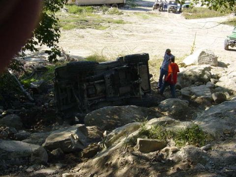 1992 Ford Bronco - An off-road vehicle has overturned in a challenging rocky environment, with onlookers observing the scene.