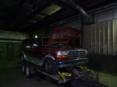 1993 Ford C-150 (Centurion Conversions) - A red Ford Bronco is parked inside a garage on a trailer with its hood open.