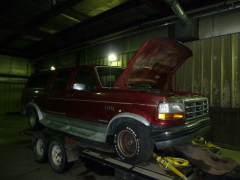 1993 Ford C-150 (Centurion Conversions) - A red SUV is loaded onto a trailer, its hood propped open, revealing the engine bay.