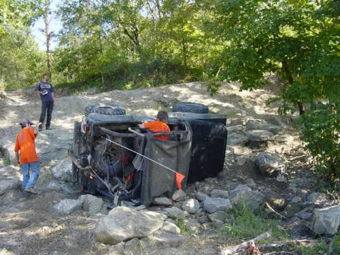1992 Ford Bronco - An off-road vehicle has overturned on a rocky trail, with two individuals observing the scene.