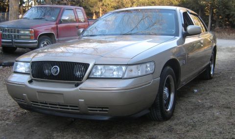 2000 Mercury Grand Marquis - A tan 2000 Mercury Grand Marquis is parked outdoors next to a red pickup truck.
