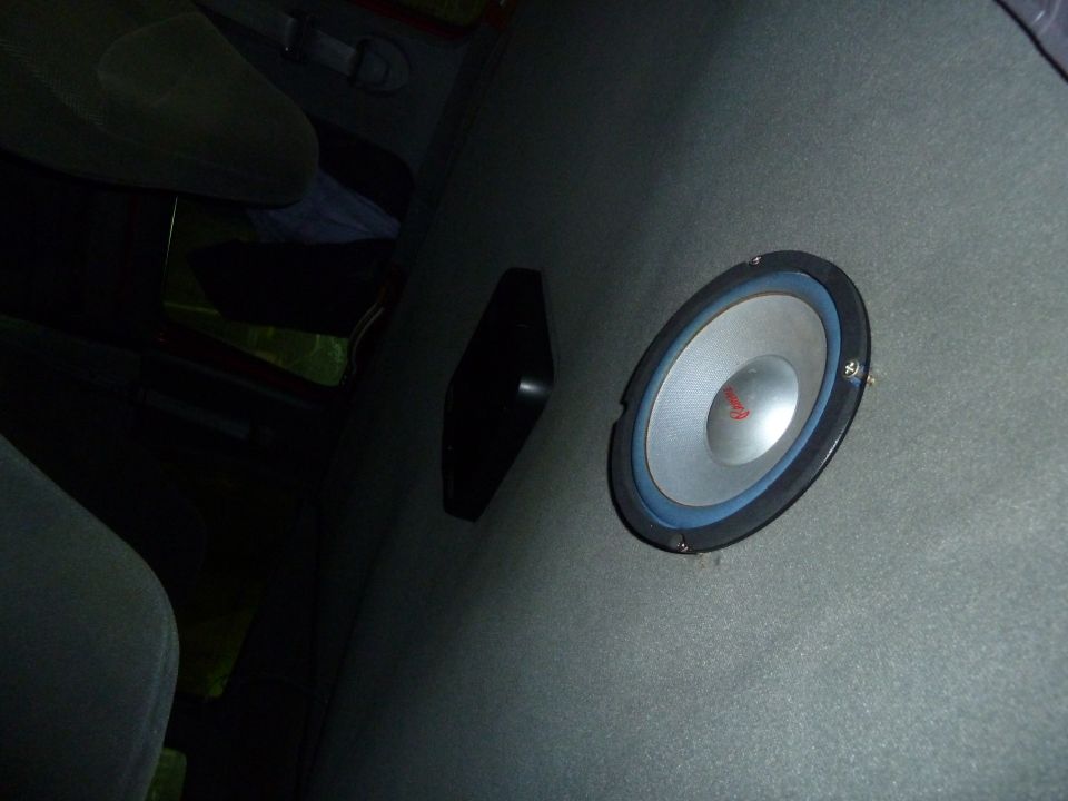 Interior view of a gray upholstered panel with a silver speaker and blue trim, next to a dark seat