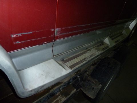 1993 Ford C-150 (Centurion Conversions) - Close-up of a red vehicle's side panel, showing wear and tear on the paint and running board.