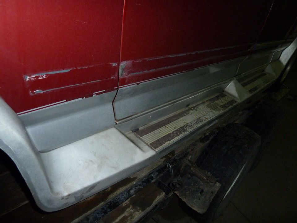 Red vehicle side with grey trim and a worn running board. Scratches are visible on the red paint above the trim