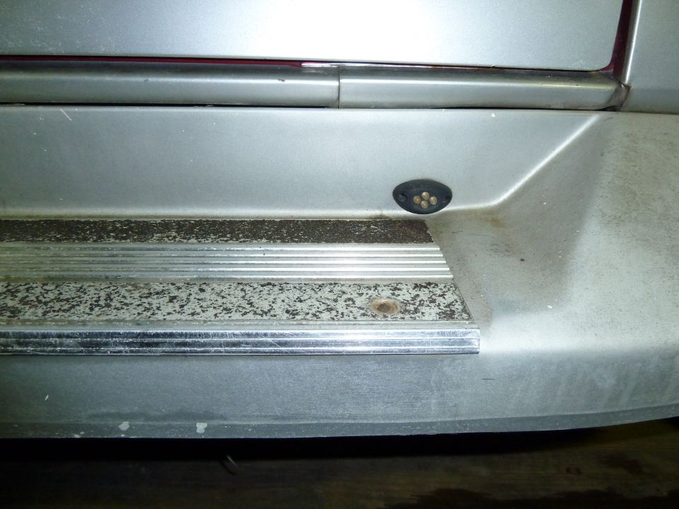 Close-up of a silver vehicle's rear bumper step with a small black housing containing four amber lights