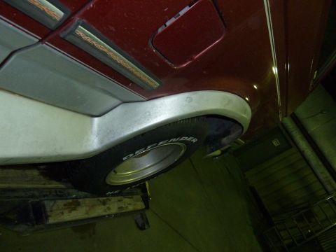 1993 Ford C-150 (Centurion Conversions) - Close-up of a red truck's side panel, showing trim details and a tire. The text "DEFENDER" is visible on the tire.