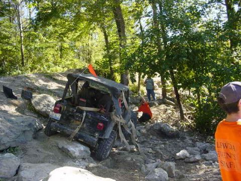 1992 Ford Bronco - A Jeep Wrangler navigates a rocky off-road trail, with people observing the challenging terrain.