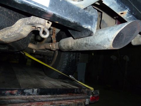 1993 Ford C-150 (Centurion Conversions) - Close-up view of a vehicle's undercarriage, focusing on the exhaust system and a tie-down strap.