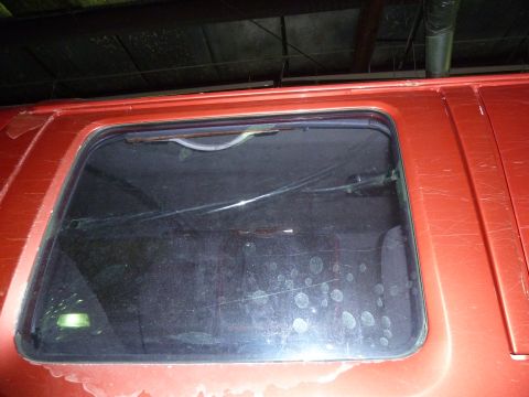 1993 Ford C-150 (Centurion Conversions) - Close-up of a red van's rear window, showing damage and dirt.