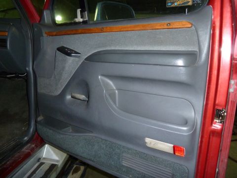 1993 Ford C-150 (Centurion Conversions) - Interior door panel of a red truck, showing gray fabric, wood trim, and storage.