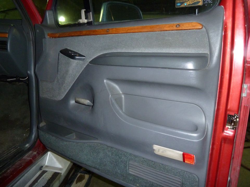 Red truck interior door panel with gray fabric and wood trim. Visible door handle, window controls, and storage pocket