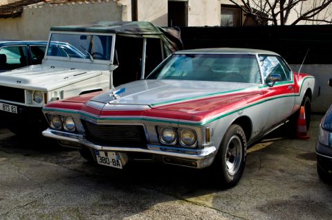 1991 Ford LTD Crown Victoria - A classic 1973 Buick Riviera with distinctive red and green racing stripes is parked next to other vehicles.