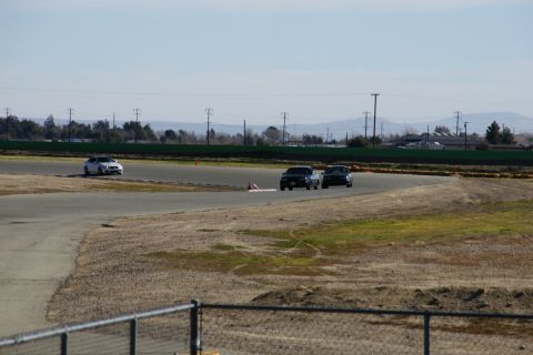 1995 Ford Taurus - Cars race on a track with a fence in the foreground and distant hills under a clear sky.