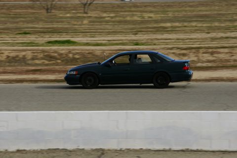 1995 Ford Taurus - A dark green 1995 Ford Taurus sedan drives along a track with a blurred background.