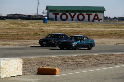 1995 Ford Taurus - Two sedans are seen on a race track with a large TOYOTA sign visible on a building in the background.