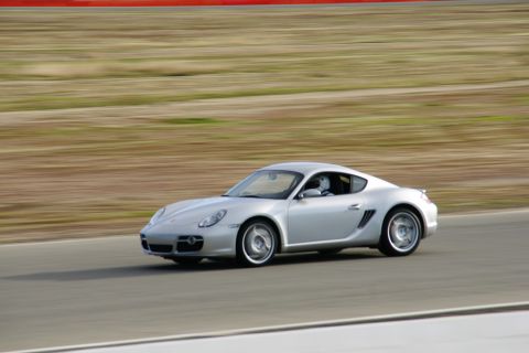 1995 Ford Taurus - A silver Porsche Cayman S drives on a race track with a blurred background.