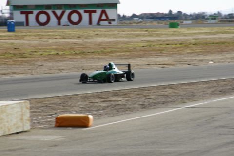 1995 Ford Taurus - A green formula racing car drives on a track with a TOYOTA building in the background.