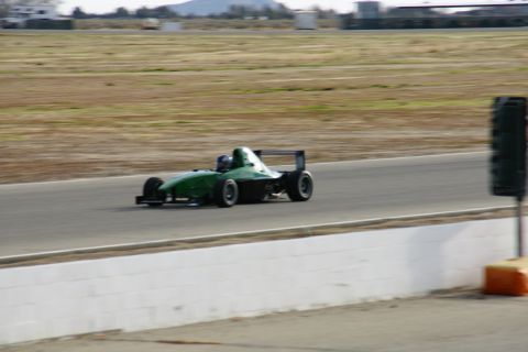 1995 Ford Taurus - A green open-wheel race car speeds down a track with a driver visible inside.