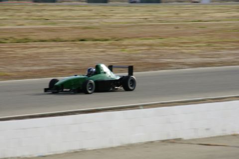 1995 Ford Taurus - A green open-wheel race car speeds along a track, its driver visible in the cockpit.