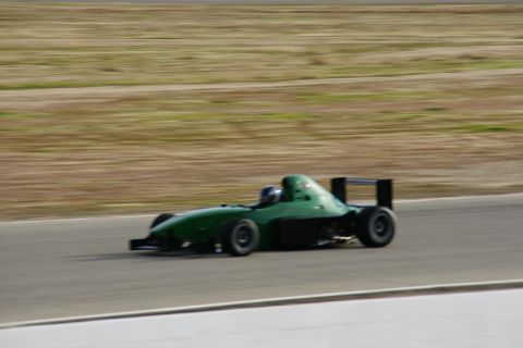 1995 Ford Taurus - A green race car speeds down a track with a blurred background of dry grass and dirt.