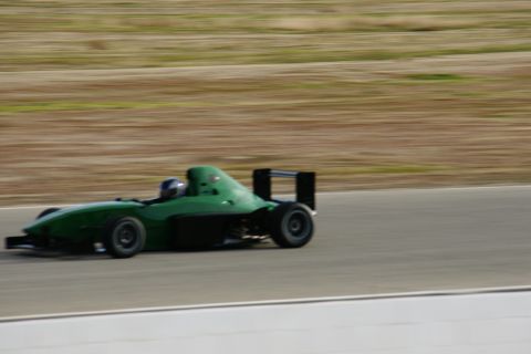 1995 Ford Taurus - A green open-wheel race car speeds along a track, its driver visible behind the wheel.