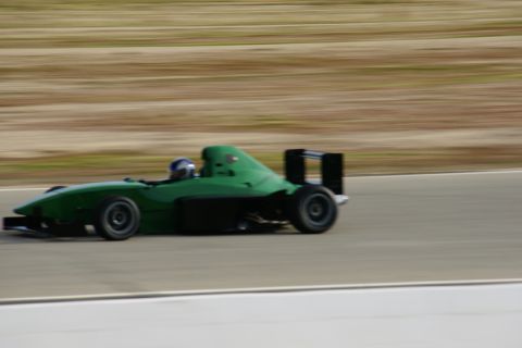 1995 Ford Taurus - A green open-wheel race car speeds along a track, blurring the background with motion.
