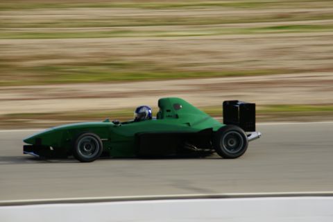 1995 Ford Taurus - Green open-wheel race car speeds down a track with a blurred background.