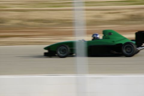 1995 Ford Taurus - A green race car speeds down a track, its driver visible in the cockpit.